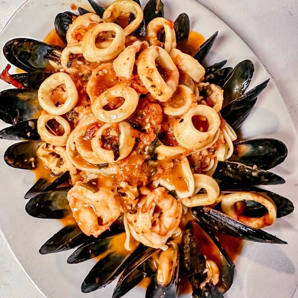 Seafood pasta with mussels, calamari, and shrimp in a rich tomato sauce on a white plate.