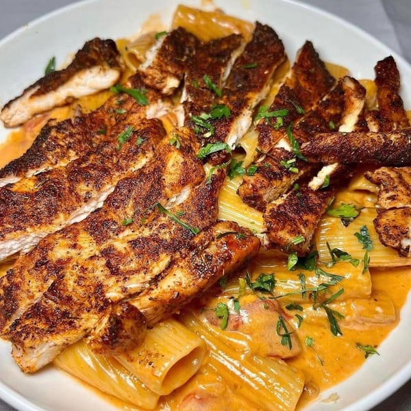 Rigatoni pasta in a creamy tomato sauce, topped with sliced blackened chicken and fresh parsley.