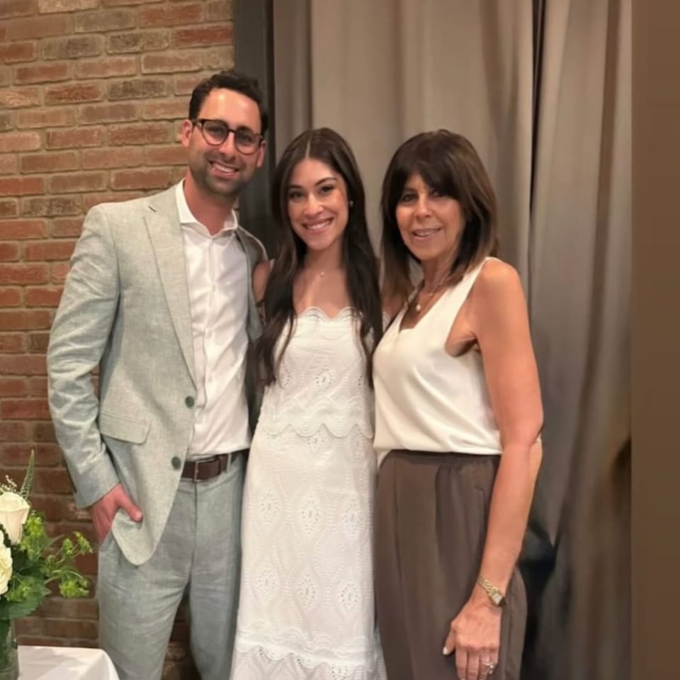 Three smiling people, two women and one man, posing together in a restaurant setting.