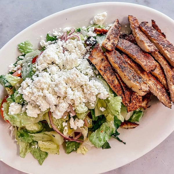 A Fig & Tomato Italian European Eatery salad with grilled chicken, lettuce, tomatoes, and feta cheese.