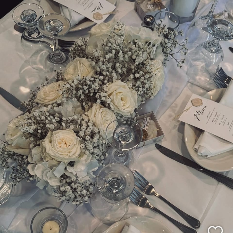Elegant table setting with white roses, baby's breath, wine glasses, and menus at Fig & Tomato.