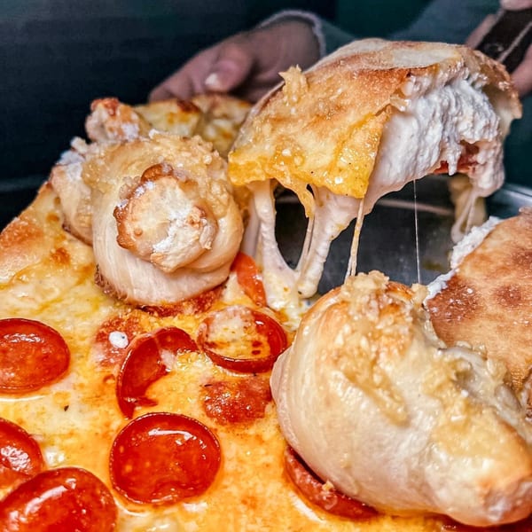 Close-up of a pepperoni pizza with cheesy garlic knots, cheese stretching from a pulled knot.