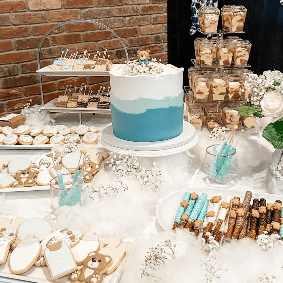 A dessert table with a blue ombre cake, teddy bear cookies, and other treats for a baby shower.