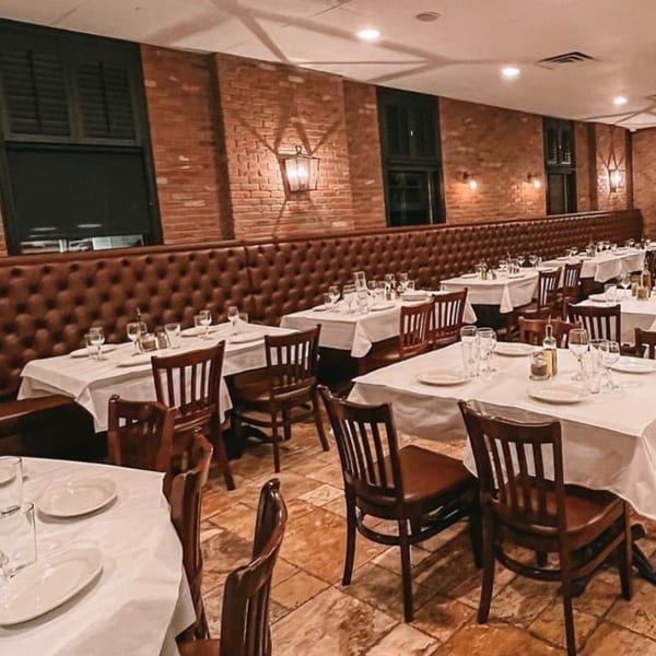 Elegant Italian European dining room with set tables, brown leather banquettes, brick walls, and warm lighting.