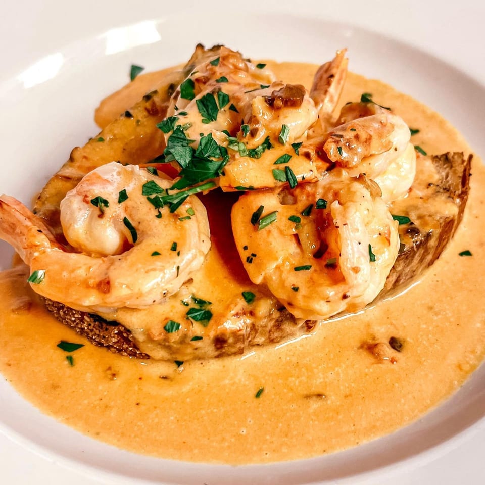 Shrimp scampi with creamy sauce and fresh parsley on toasted bread, served on a white plate.