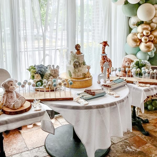 Safari-themed baby shower dessert table with a two-tier cake, cake pops, and animal decorations.