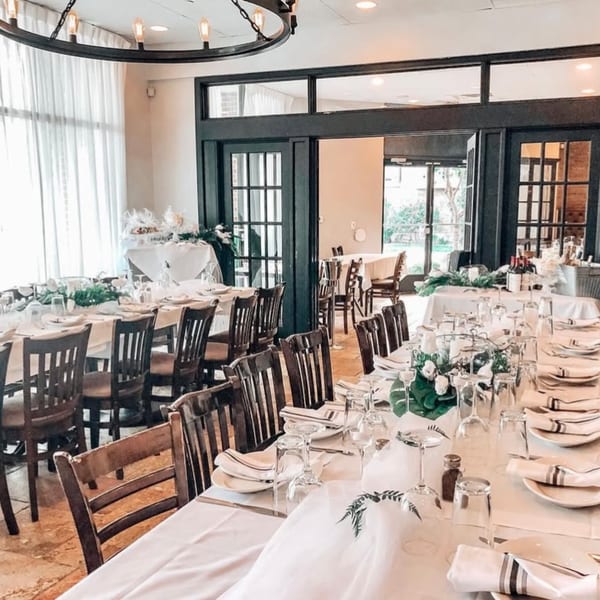 Long dining tables set with white tablecloths, place settings, and floral centerpieces in a bright room.
