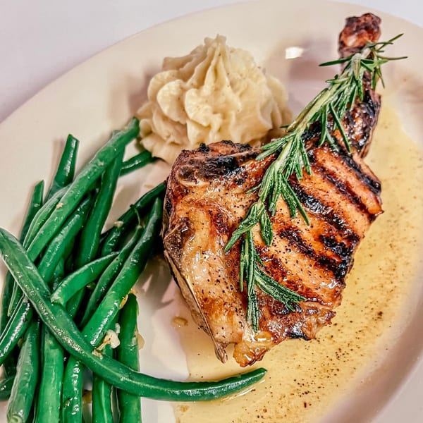 Grilled pork chop with rosemary, mashed potatoes, and green beans on a white plate.