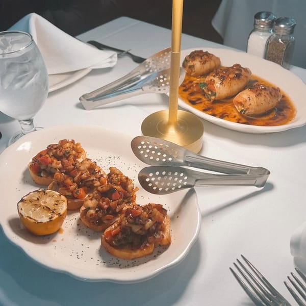 Italian appetizers: bruschetta with grilled lemon and stuffed calamari in sauce on a white tablecloth.