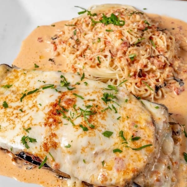 Eggplant parmesan with melted cheese and a side of spaghetti in a creamy tomato sauce.