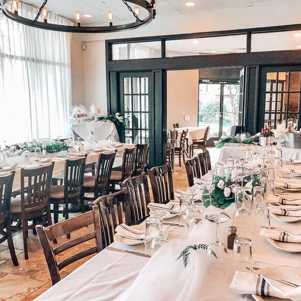 Elegant dining room at Fig & Tomato with long tables set for a banquet, featuring white linens and dark wood chairs.