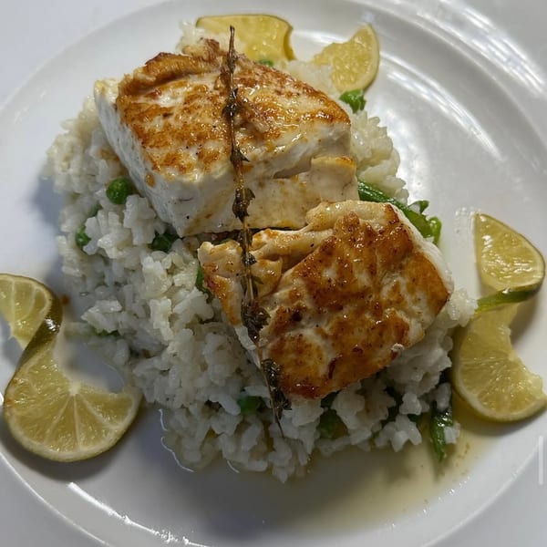 Pan-seared fish over white rice with green peas, garnished with lime wedges and a thyme sprig.