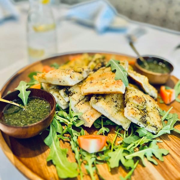 Focaccia bread with pesto, arugula, and tomato on a wooden serving board at Fig & Tomato.