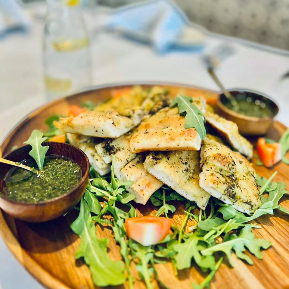 Focaccia bread with pesto, arugula, and tomato on a wooden serving board at Fig & Tomato.