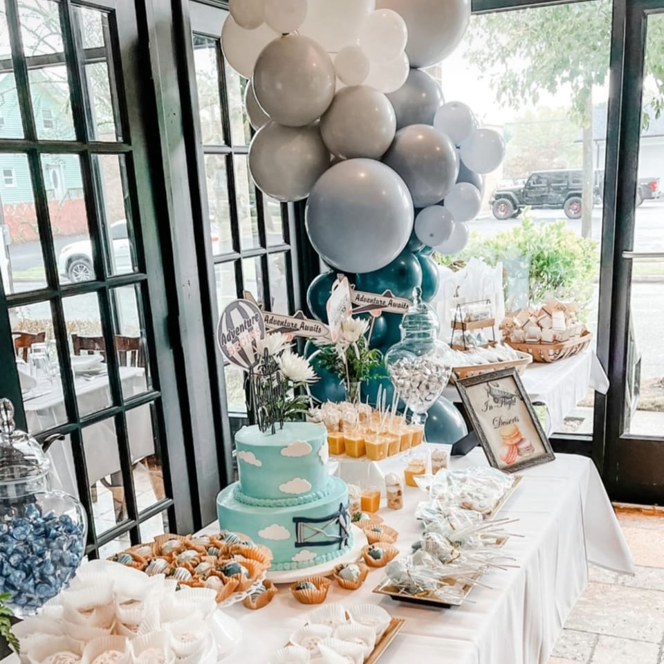 A dessert table with a blue cake, various sweets, and balloons at Fig & Tomato.