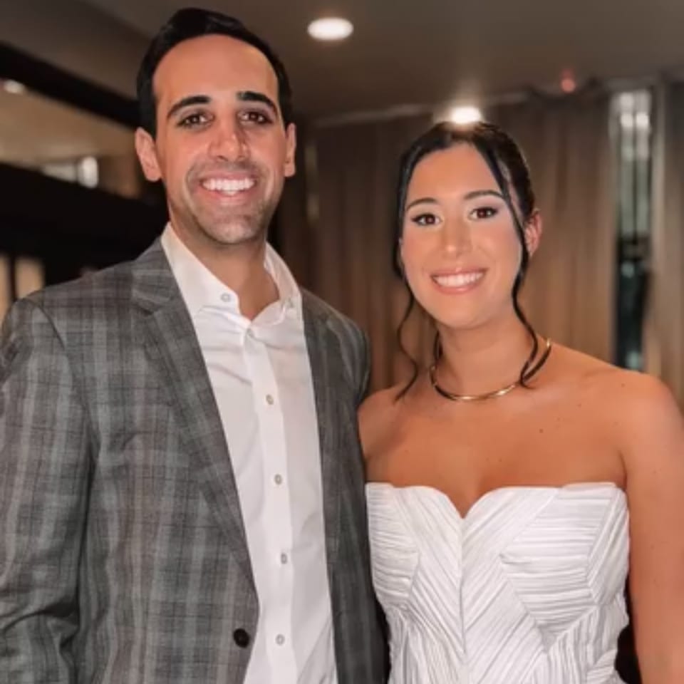 Smiling man in a plaid suit and woman in a white strapless dress with a gold choker.