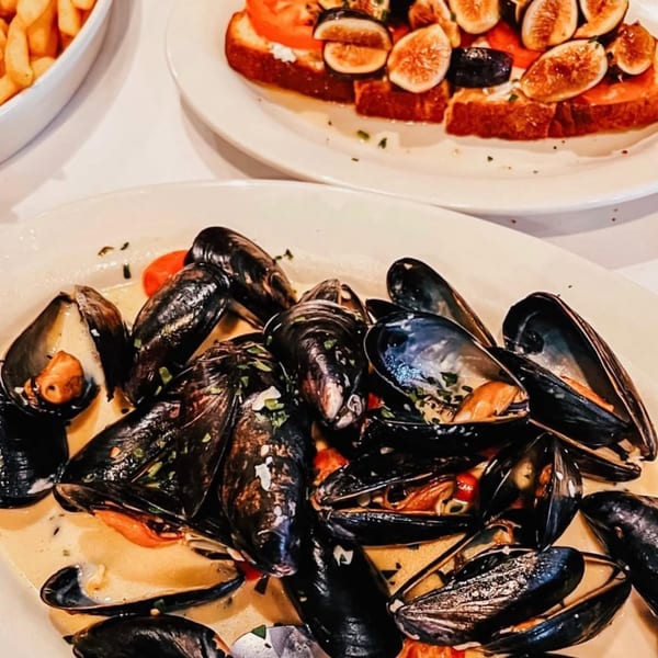 Steamed mussels in a creamy sauce, with a fig and tomato bruschetta in the background.