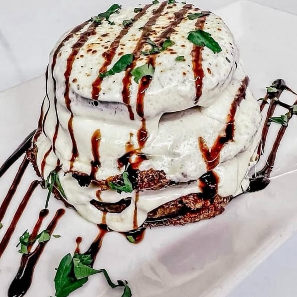 Stacked eggplant parmesan with melted cheese, balsamic glaze, and fresh basil on a white plate.
