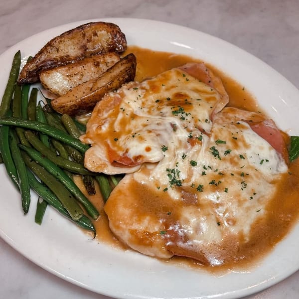 Chicken Saltimbocca with melted cheese, prosciutto, gravy, green beans, and roasted potato wedges.