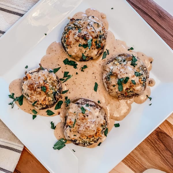 Four stuffed mushrooms with creamy sauce and fresh parsley on a white plate at Fig & Tomato.