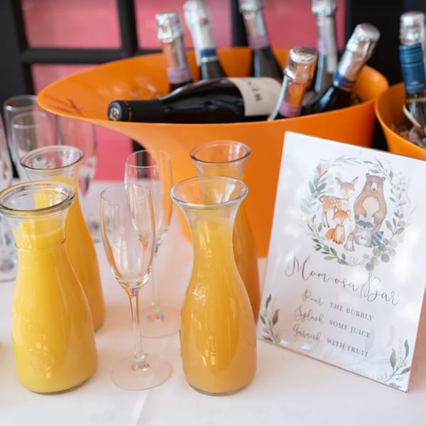 A mimosa bar with carafes of orange juice, champagne bottles in an orange bucket, and flutes.