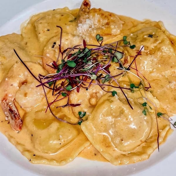 Shrimp ravioli in a creamy sauce, garnished with microgreens and grated cheese.