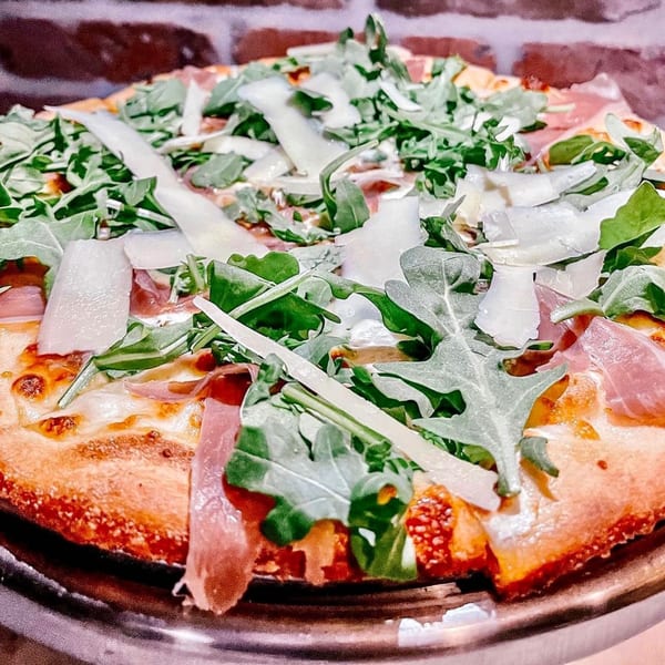 A Fig & Tomato Italian pizza topped with prosciutto, fresh arugula, and shaved Parmesan cheese.